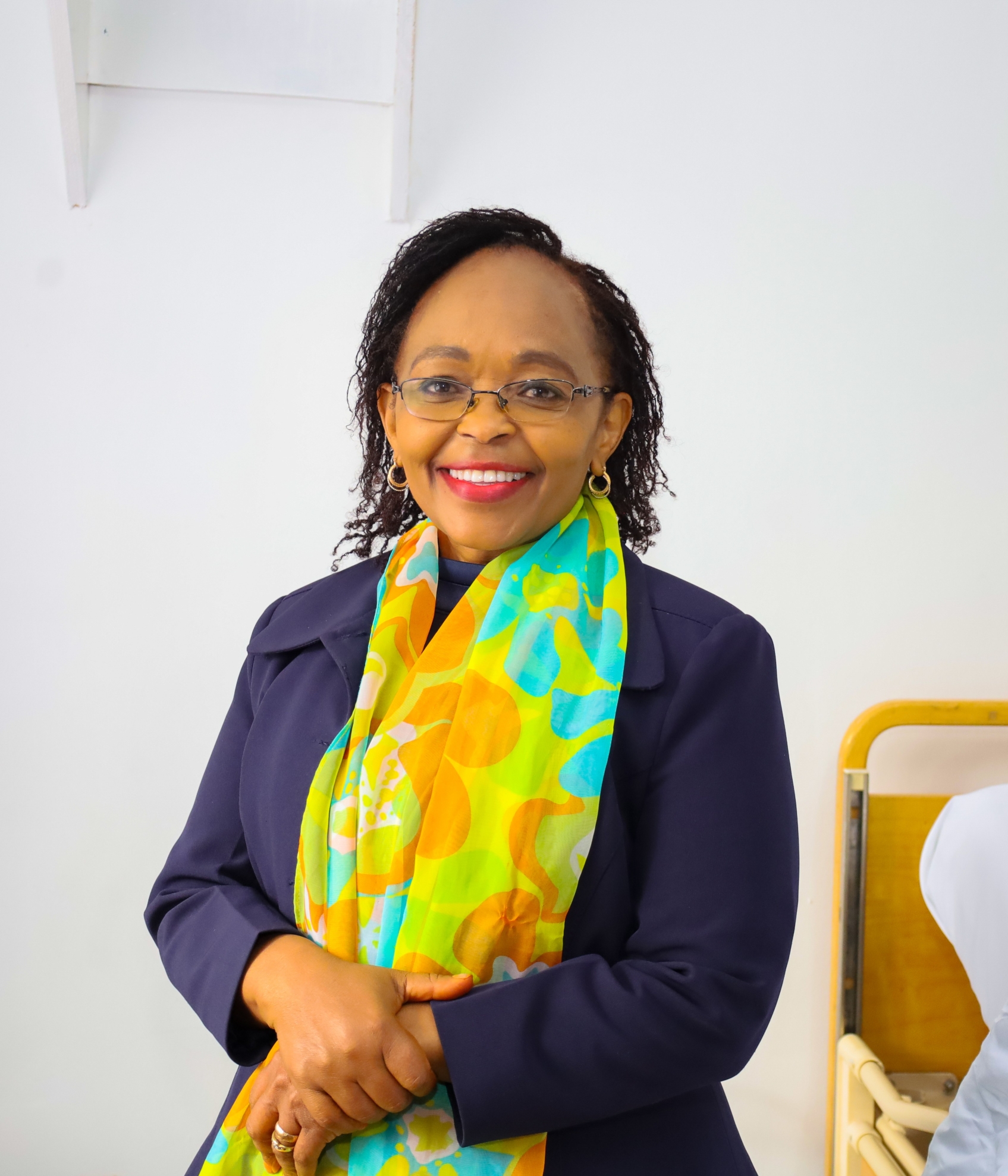 Professional portrait of Faith Malavu smiling confidently in formal attire, standing in a modern healthcare or office setting, representing leadership, compassion, and professionalism in healthcare services.
